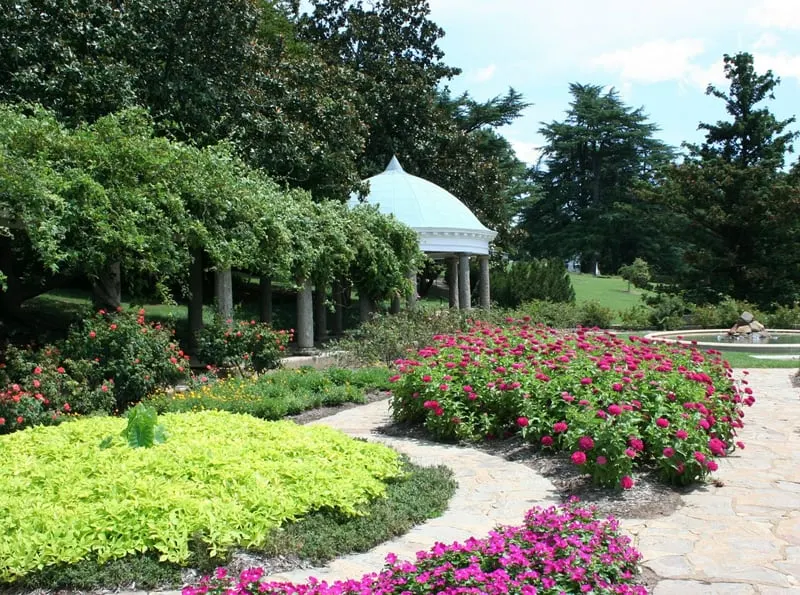 This flagstone garden walkway goes around gorgeous red and pink flowers, as well as fresh green ground covers, creating a peaceful setting.