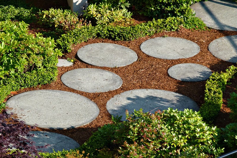 Round shaped, different sized concrete tiles surrounded by mulch, make this a visually appealing walkway.