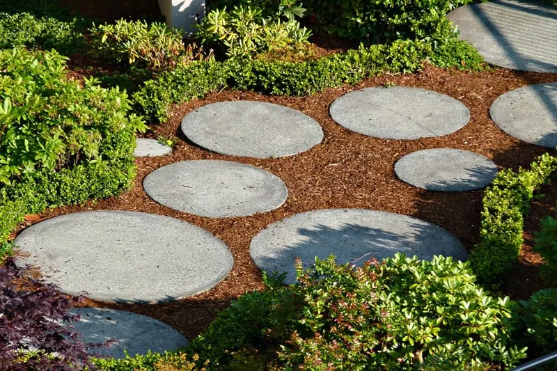 Round shaped, different sized concrete tiles surrounded by mulch, make this a visually appealing walkway.