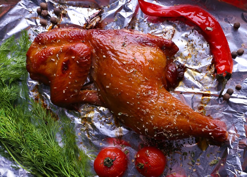 Smoked chicken leg with cherry tomatoes on foil close up