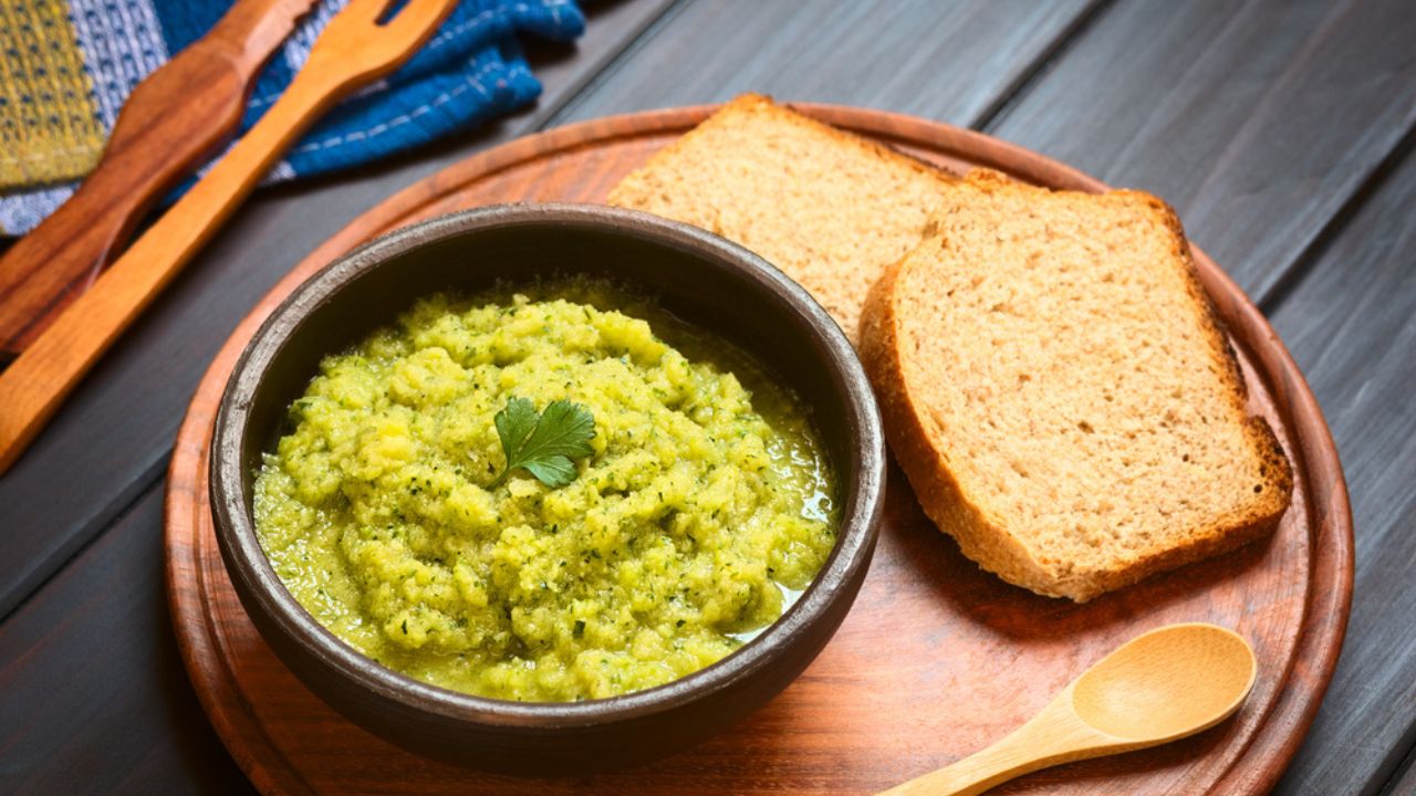 Homemade zucchini and parsley spread garnished with fresh parsley leaf, slices of wholegrain bread on the side, photographed on dark wood