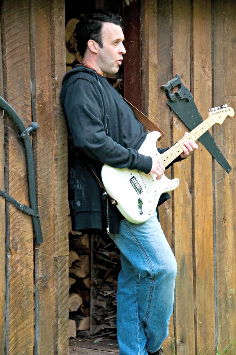 Man playing his guitar in front of his man cave shed