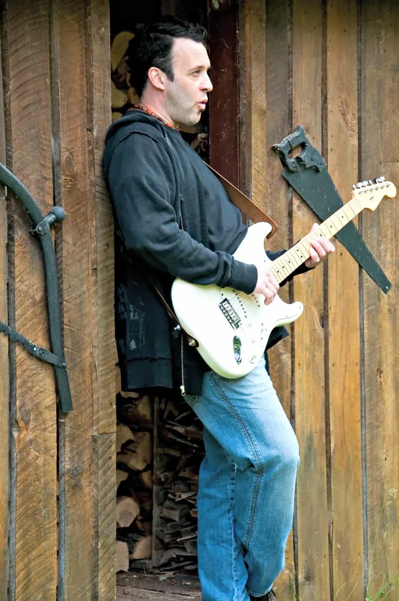 Man playing his guitar in front of his man cave shed