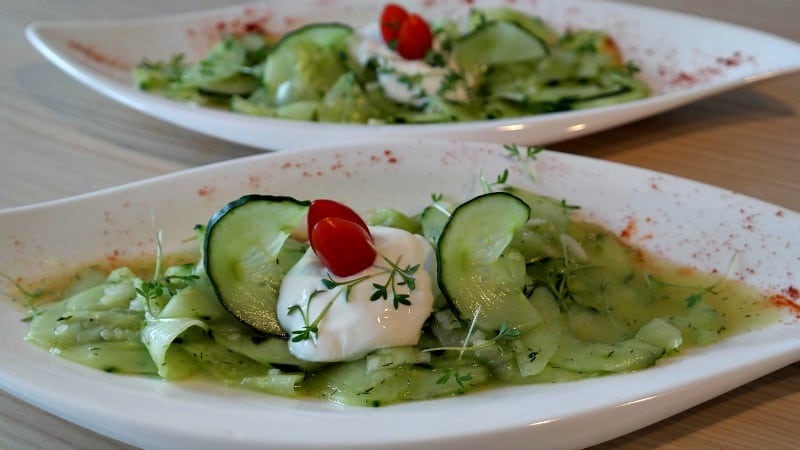 A bowl of cucumber salad with a dollop of sour cream and herbs on a white plate