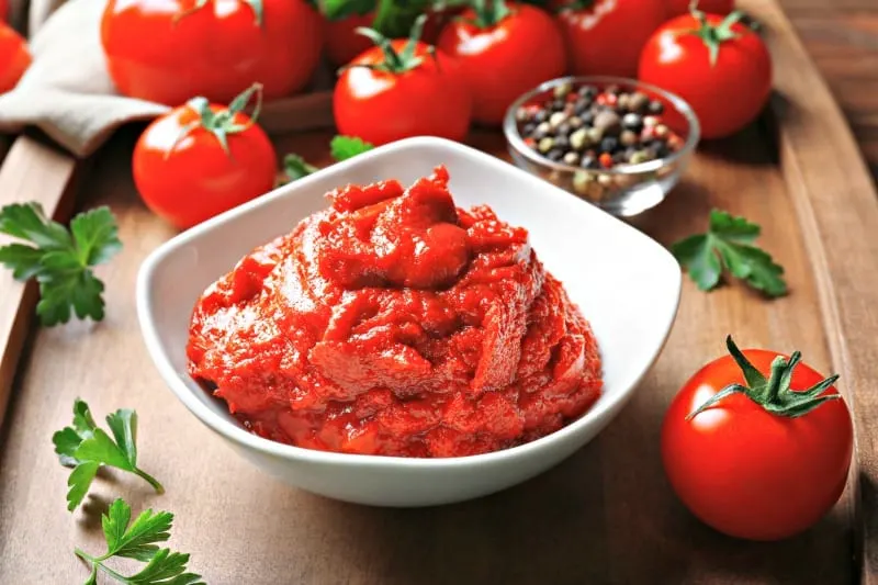 Delicious tomato paste in bowl with ingredients on tray
