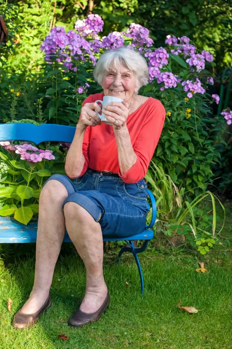 Grandma enjoying a cup of tea on a bench in her garden