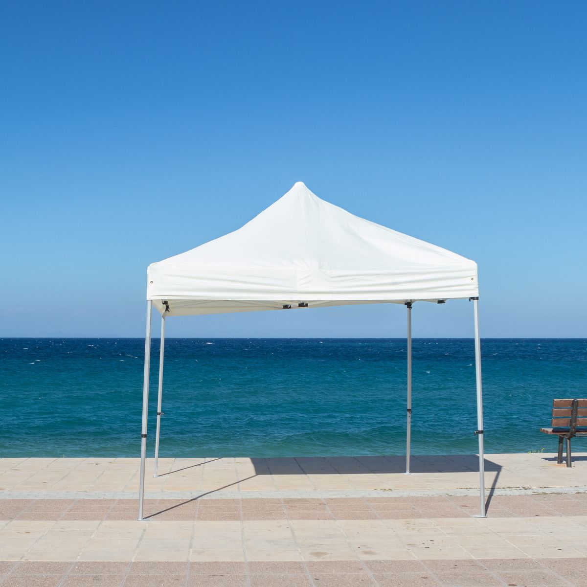 A pop up gazebo is seen on a coastal walkway, shelter from the hot summer sun, blue hues are seen in background with copy space.