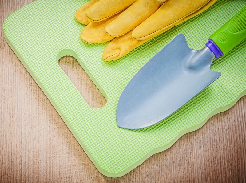 Safety gloves, garden knee mat and a hand spade on wooden board