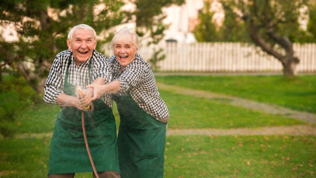 old couple having fun with a water hose in the backyard.