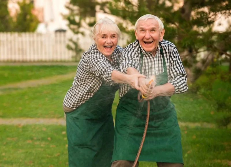 Old couple having fun. Happy people with garden hose.