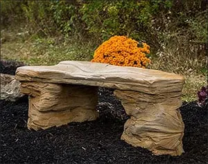 A bench made from solid rock and an orange flower bouquet behind it