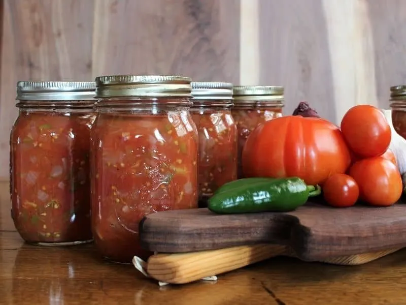 Canned salsa jars and tomatoes on a table