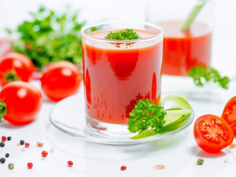 Tomato juice in glass surrounded by tomatoes, basil and spices