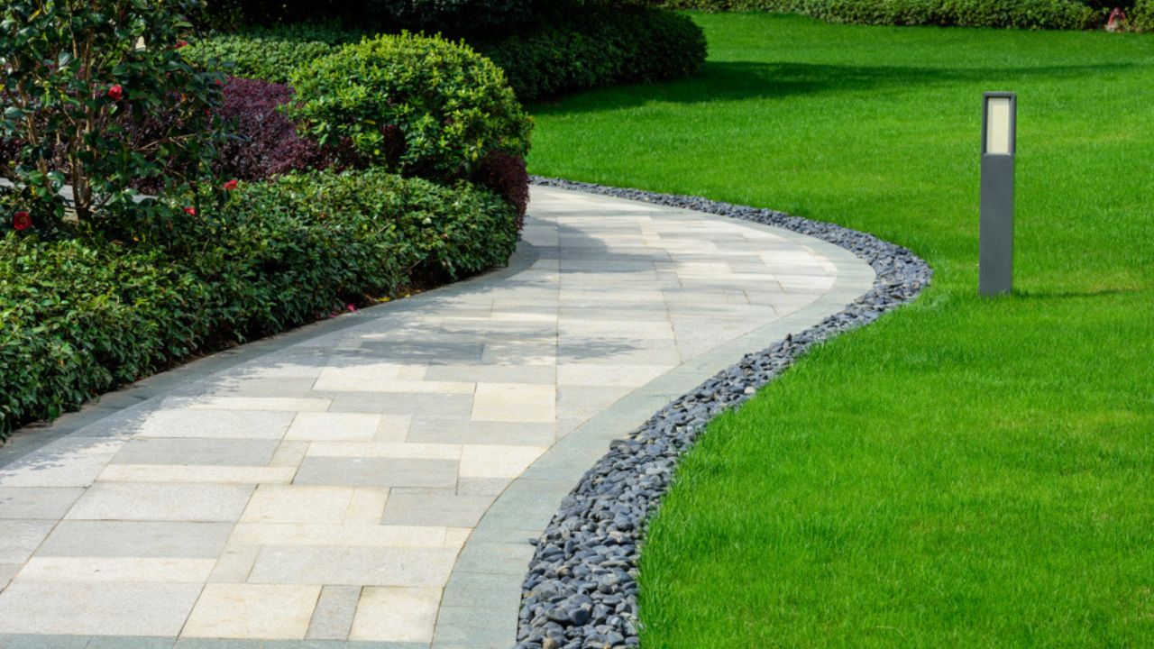 There is a black stone garden on the edge of the curved path, and the landscape lamp is on the green lawn.