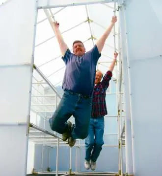 A couple of men hanging onto a Solexx greenhouse frame