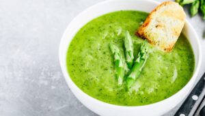 Asparagus cream soup with croutons on gray stone background. Green summer vegetable soup.