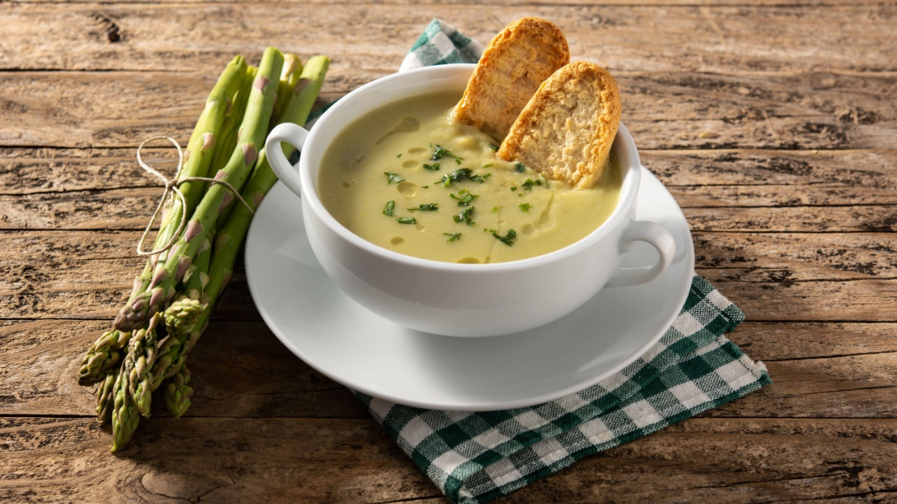 Fresh green asparagus soup in bowl on wooden table