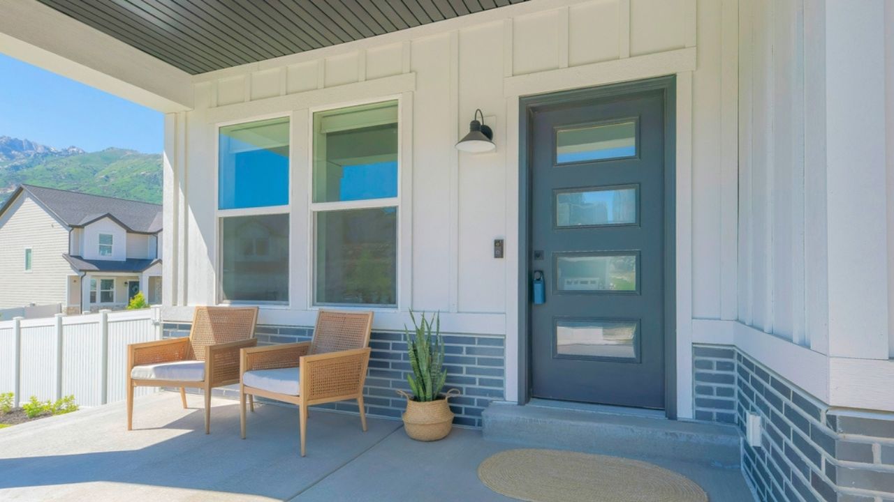 Panorama Porch with two woven armchairs and snake plant on a woven pot. Entrance exterior with black front door with glass panels