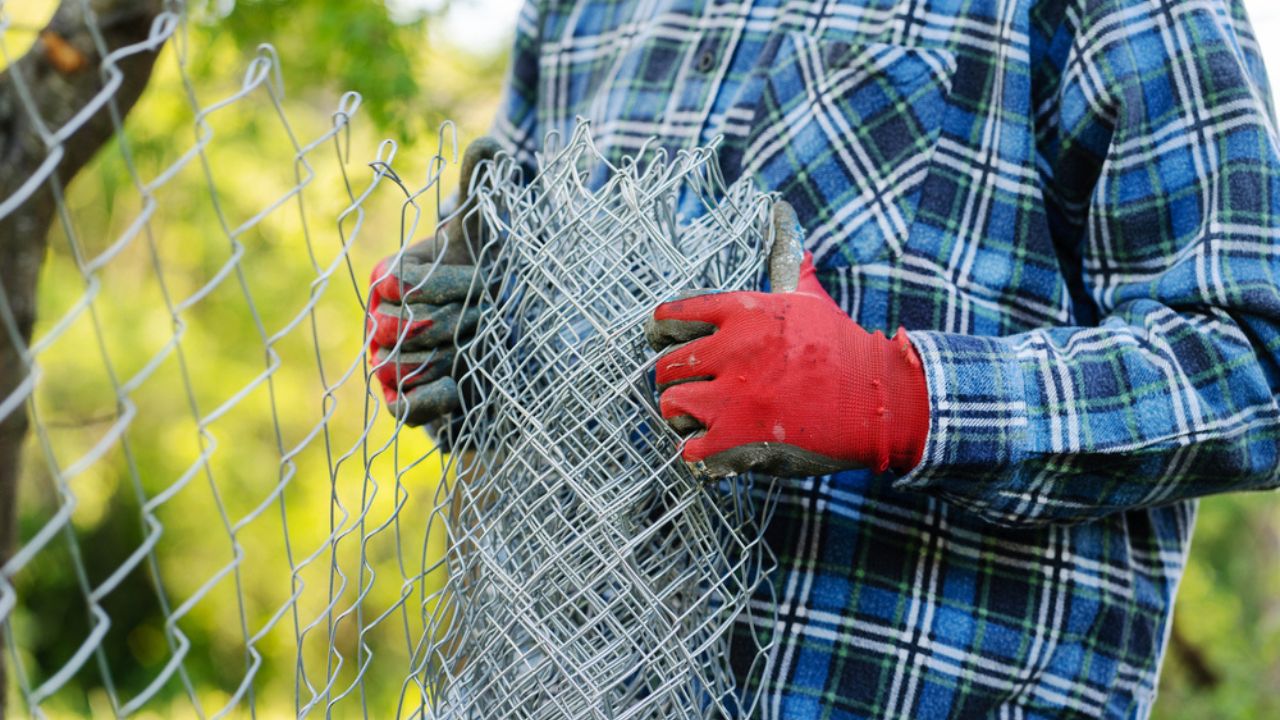 Close up on midsection of unknown man holding protective chain link diamond wire fence in the field in day with copy space