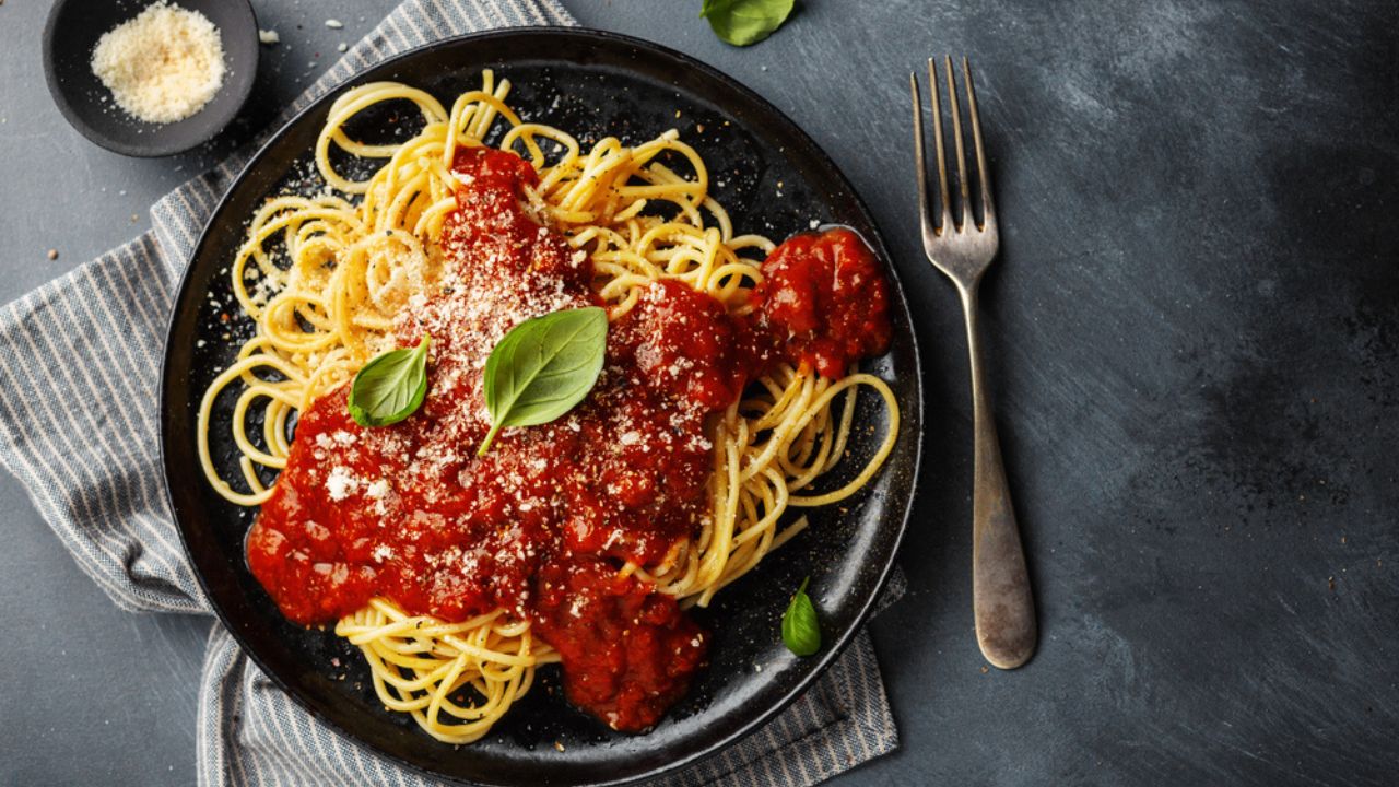 Tasty appetizing spaghetti pasta with tomato sauce served on plate on dark background.