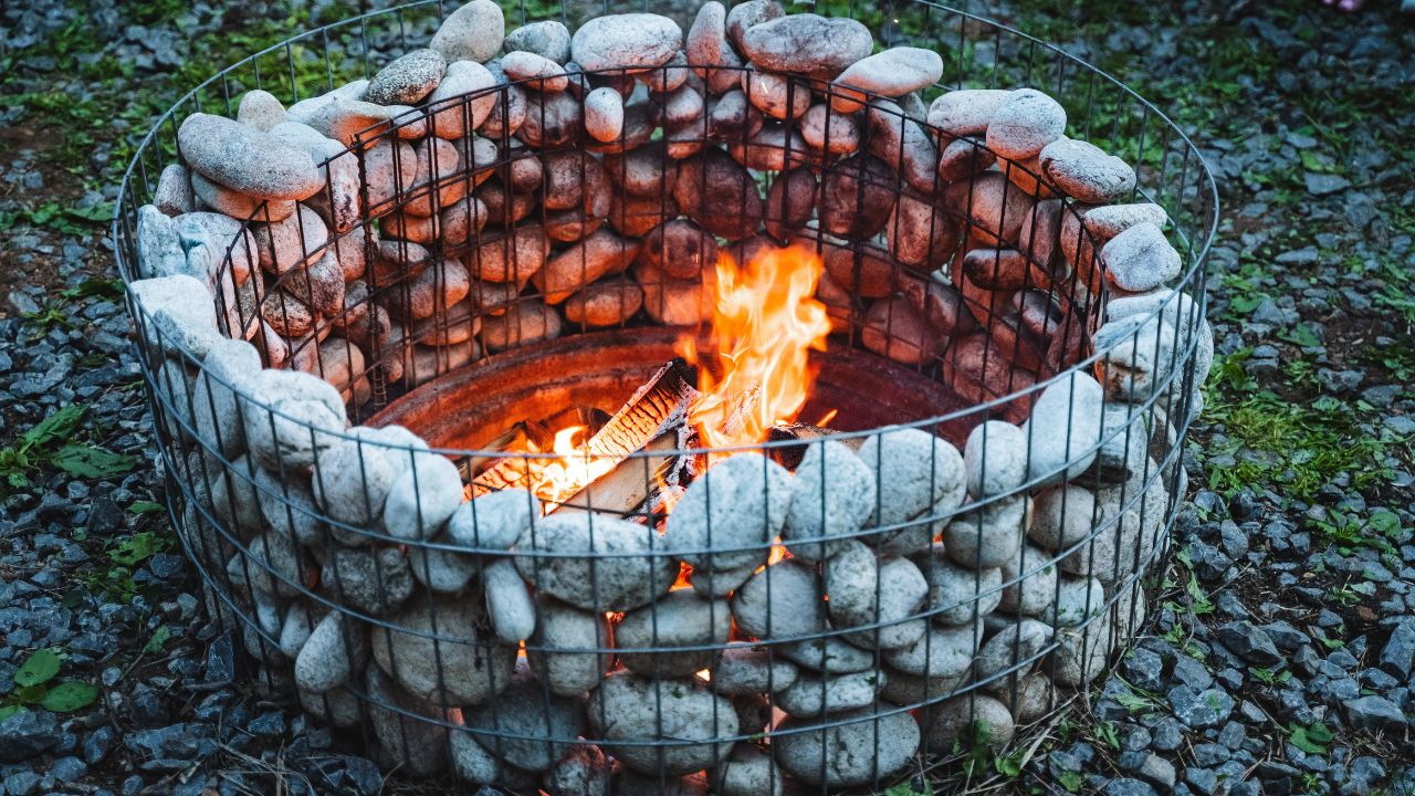 An inviting outdoor stone fire pit with a roaring fire, made of large pebbles and rocks. Perfect for backyard gatherings and cozy evenings with friends by the warm, rustic fireplace