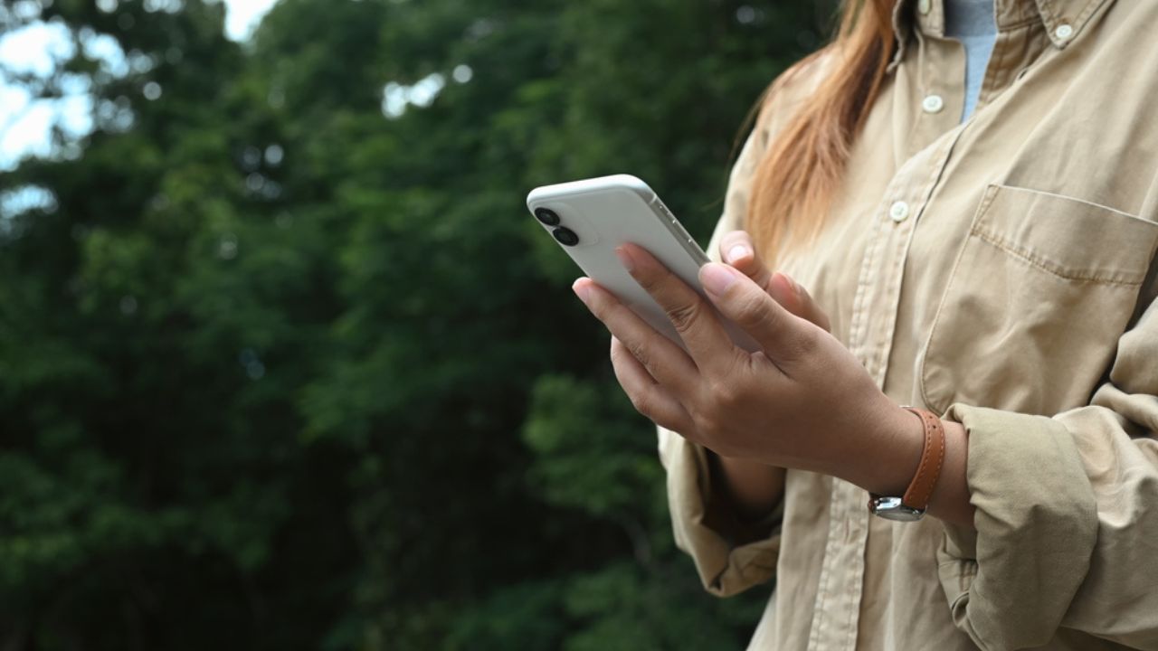 Young woman using mobile phone on green natural backdrop of trees. People, lifestyle and technology concept