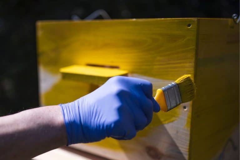 man painting a beehive yellow
