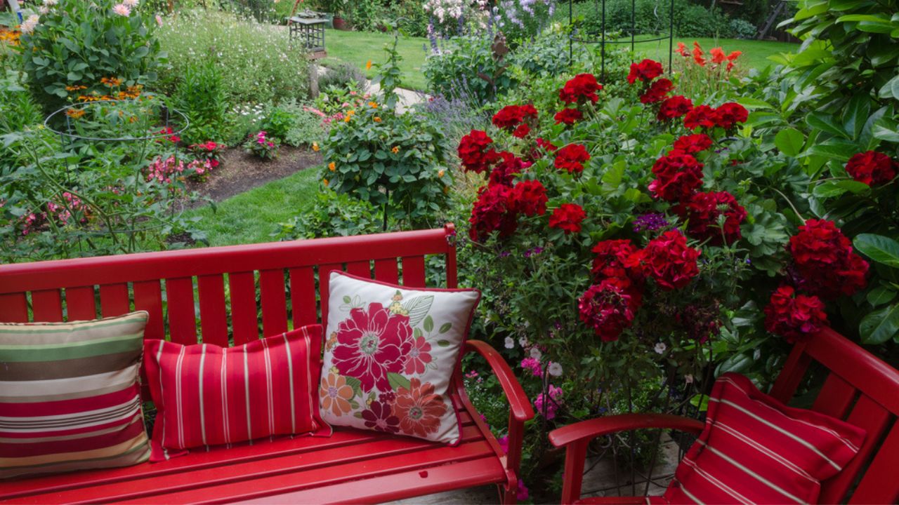 Overlooking a colorful backyard garden with casual red furniture and geraniums.in the foreground.