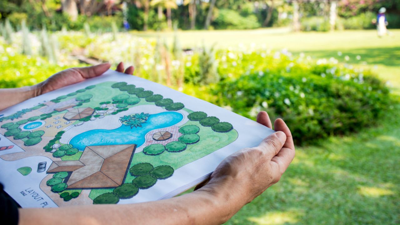 Paper sheet of layout plan with hands and garden background, that shown design of clubhouse landscape or garden design drawing by hand