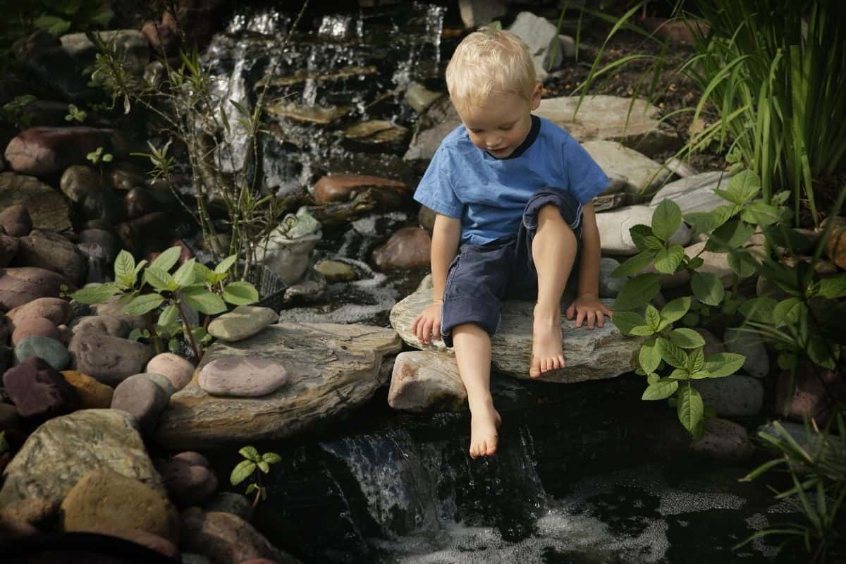 young boy playing in a water stream flowing through the backyard