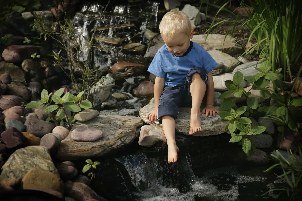 young boy playing in a water stream flowing through the backyard