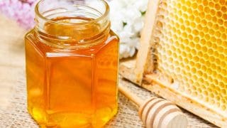 a glass jar of honey and a honeycomb in the background