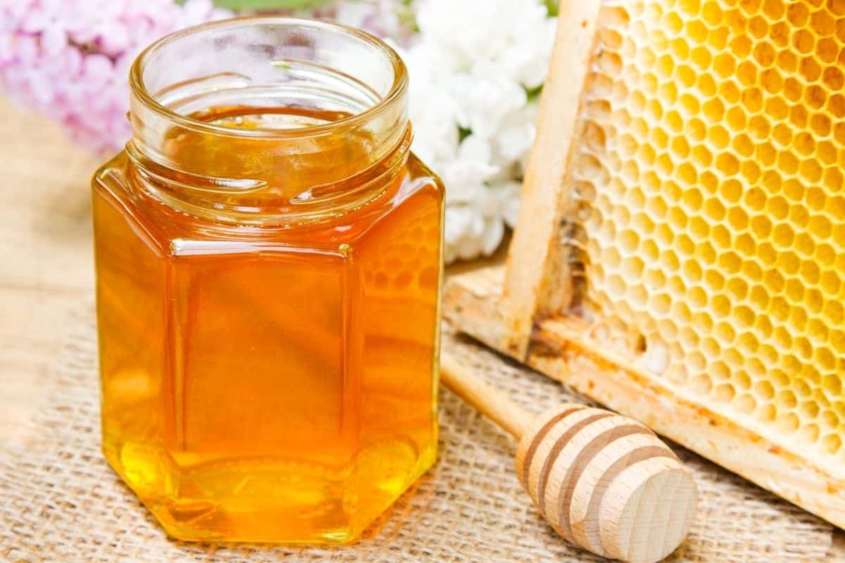 a glass jar of honey and a honeycomb in the background