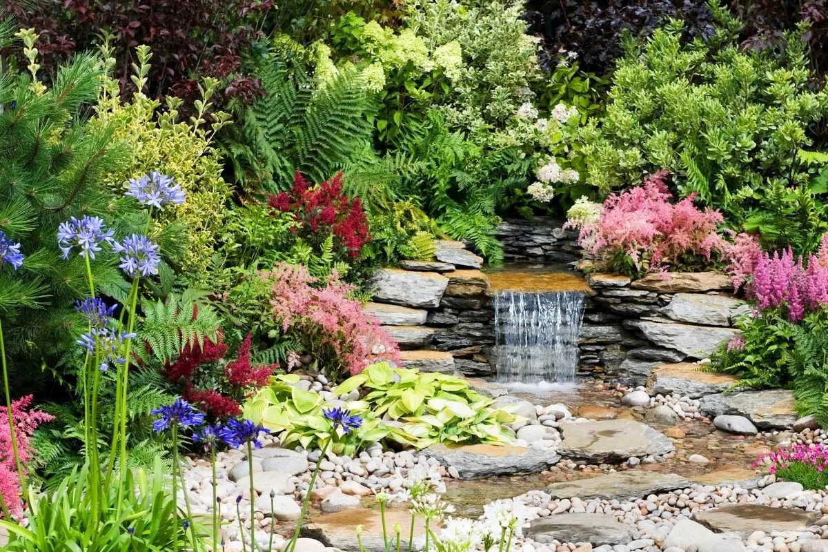 a beatiful man made waterfall surrounded by rocks and colorful flowers