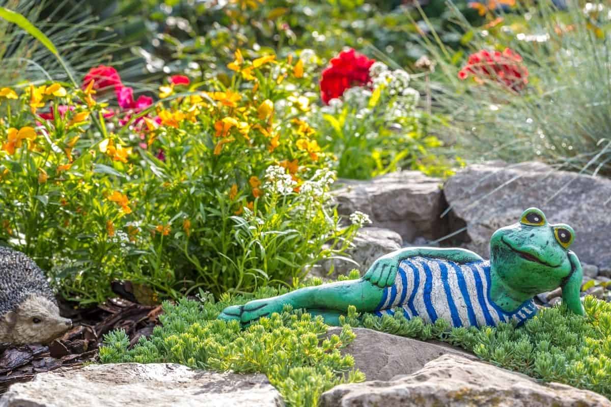 cute frog statue laying down in the flower garden