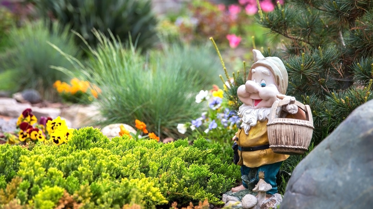 Funny garden gnome standing among nice flowers