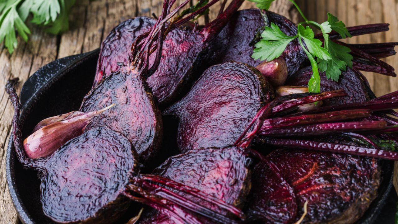 Homegrown roasted beets and garlic in cast iron skillet, fresh parsley herbs on wooden rustic table, plant based food, local produce, close up. Organic vegetables, healthy vegan eating, harvest