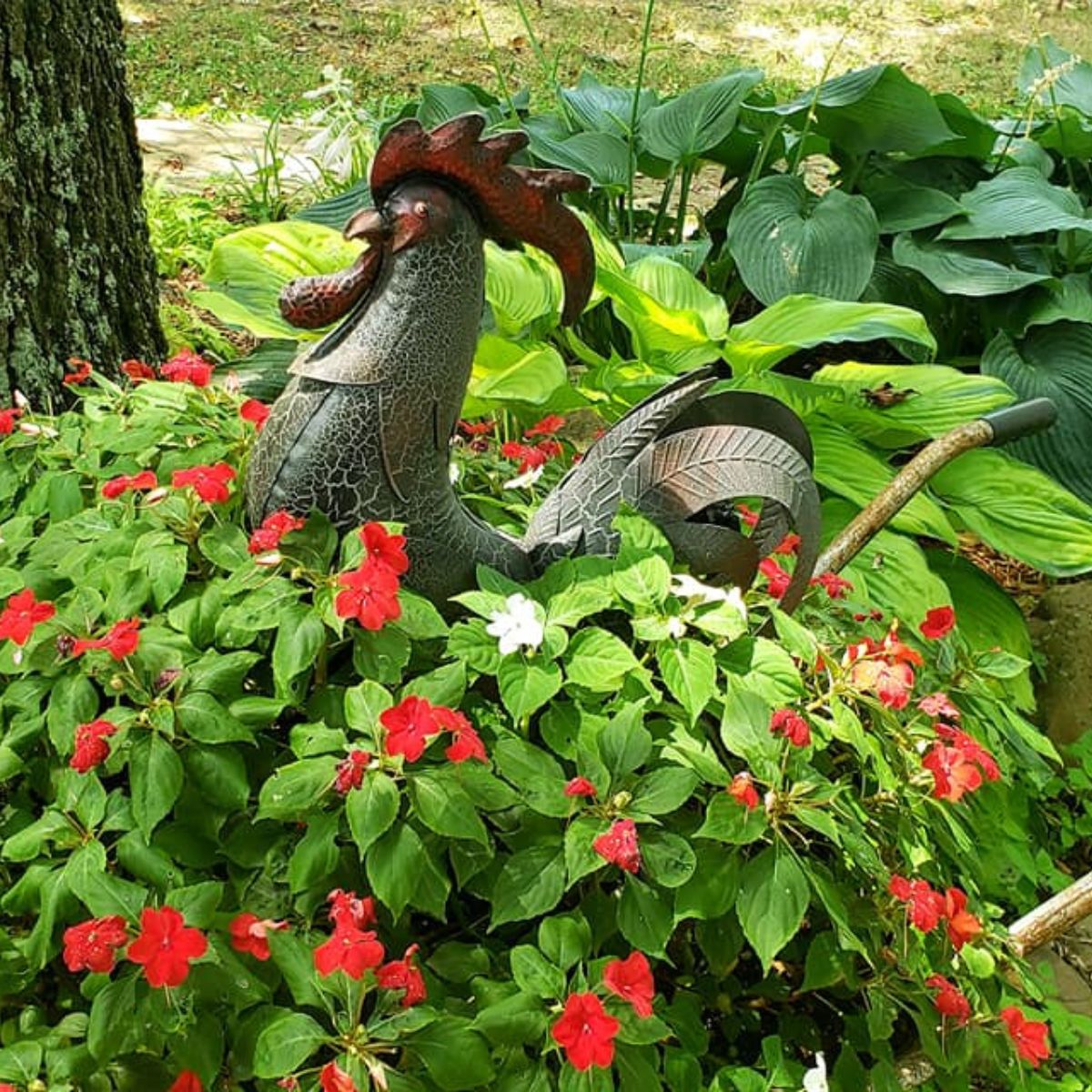 metal rooster nestled in between red impatiens