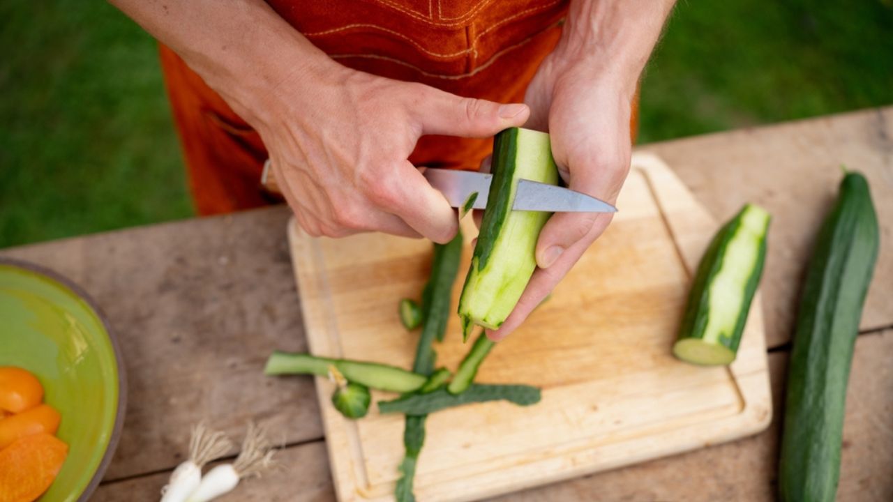 Close up of man holding sharp knife, peeling cucumber. Preparing vegetables for an outdoor barbecue.
