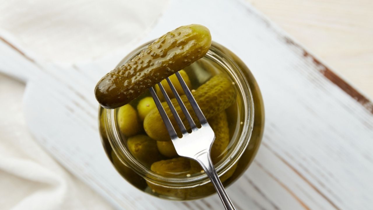 Pickled cucumbers on a fork and in a jar on a wooden background. Pickled cucumbers on a fork and in a jar on a wooden background.