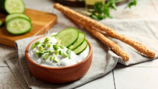 Delicious yogurt, green onion, cucumbers and grissini on light tiled table, closeup