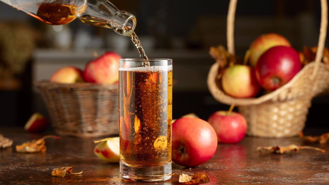 Apple cider is poured from a bottle into a glass. Fresh drink with apples on an old kitchen table.