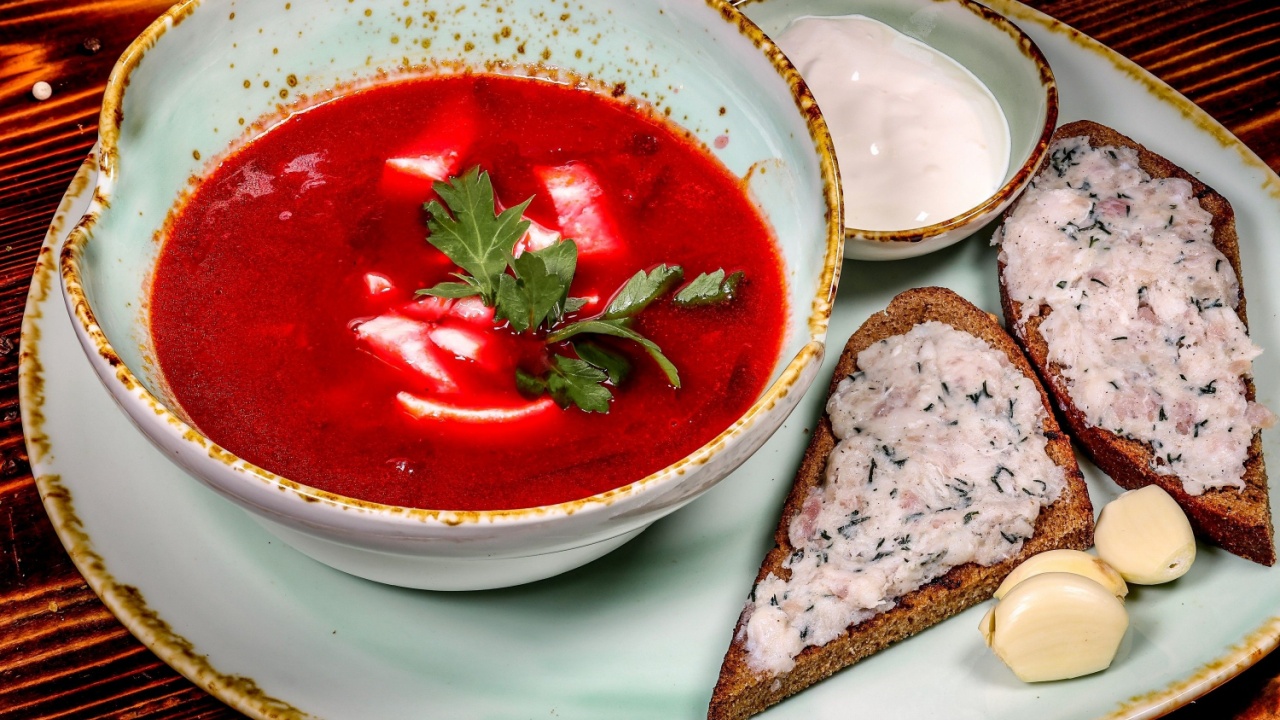 Bowl with beet borscht, creamy sauce, bread with minced lard and garlic. Rustic presentation, angle side view. Dark wooden background.