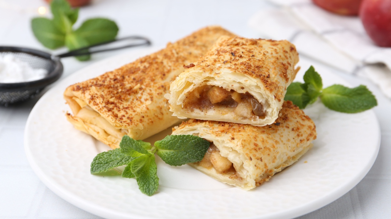 Tasty apple strudels and mint on white table, closeup