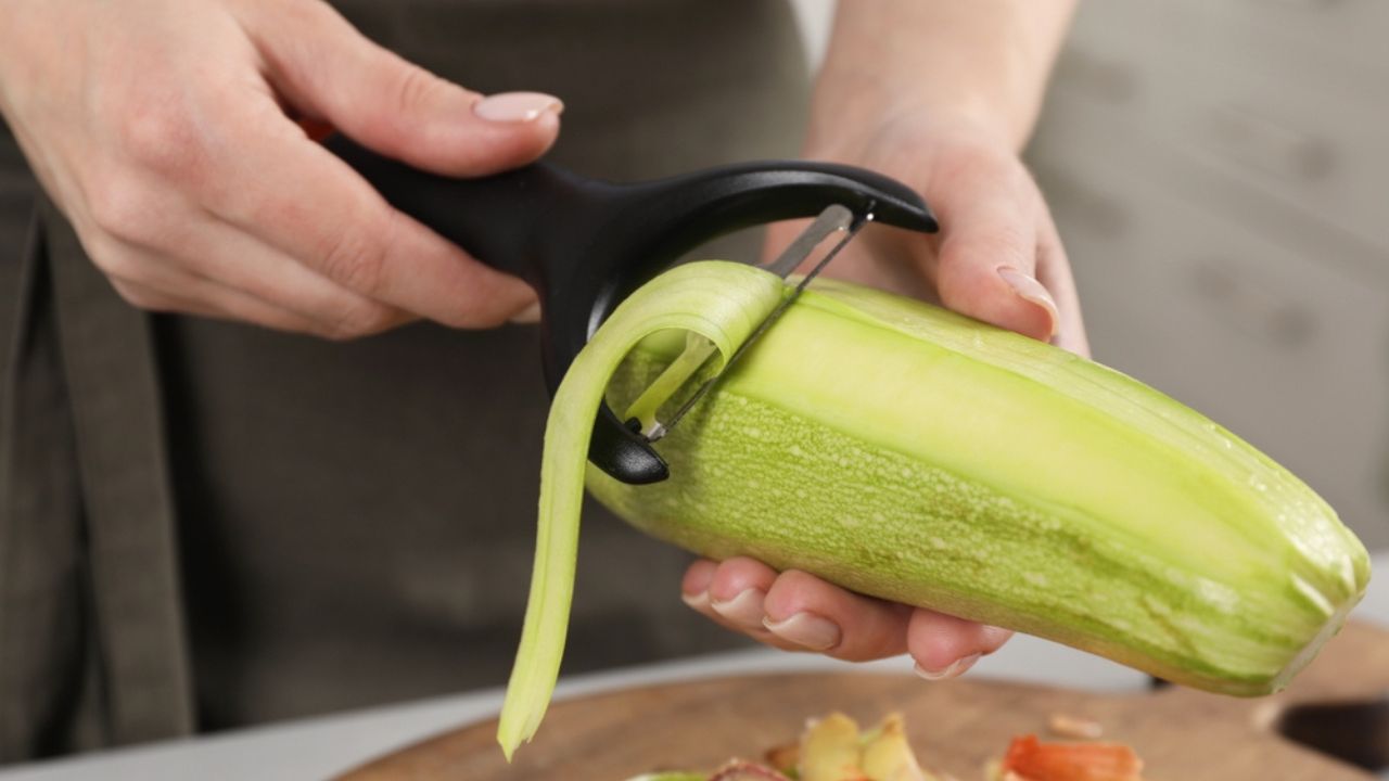 Woman peeling fresh zucchini at table indoors, closeup