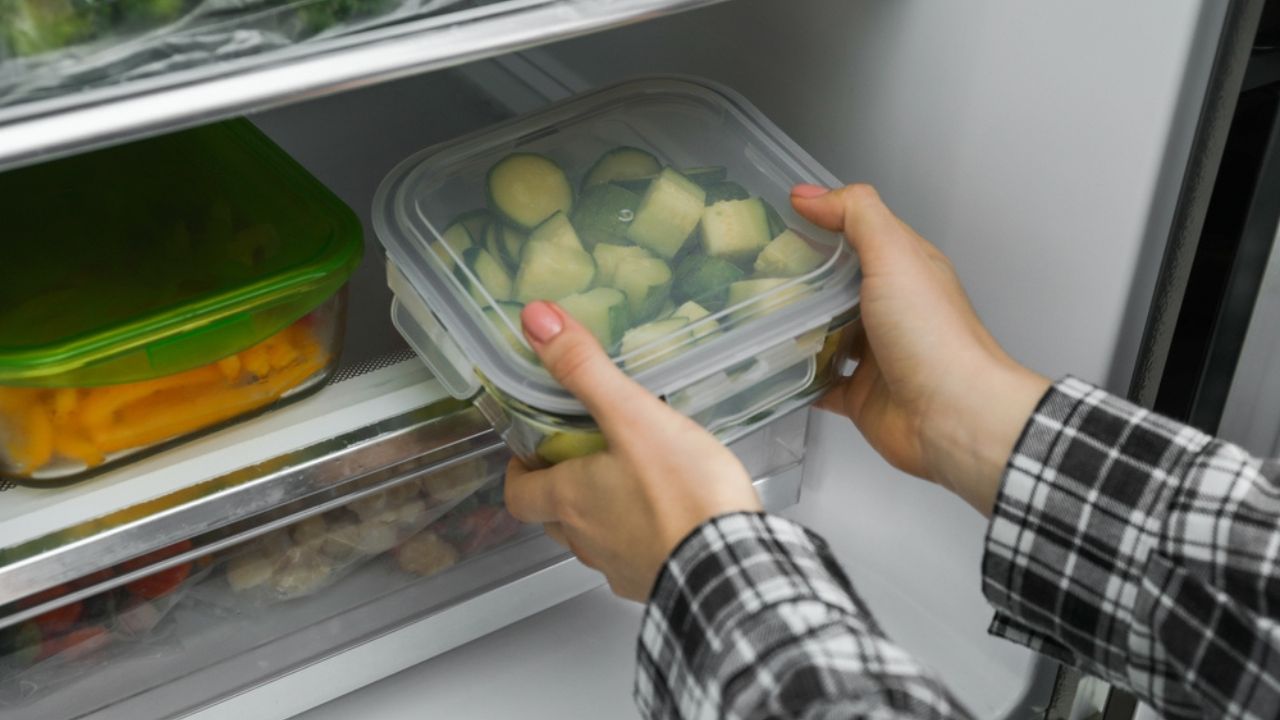 Woman taking glass container with frozen chopped zucchini from refrigerator, closeup