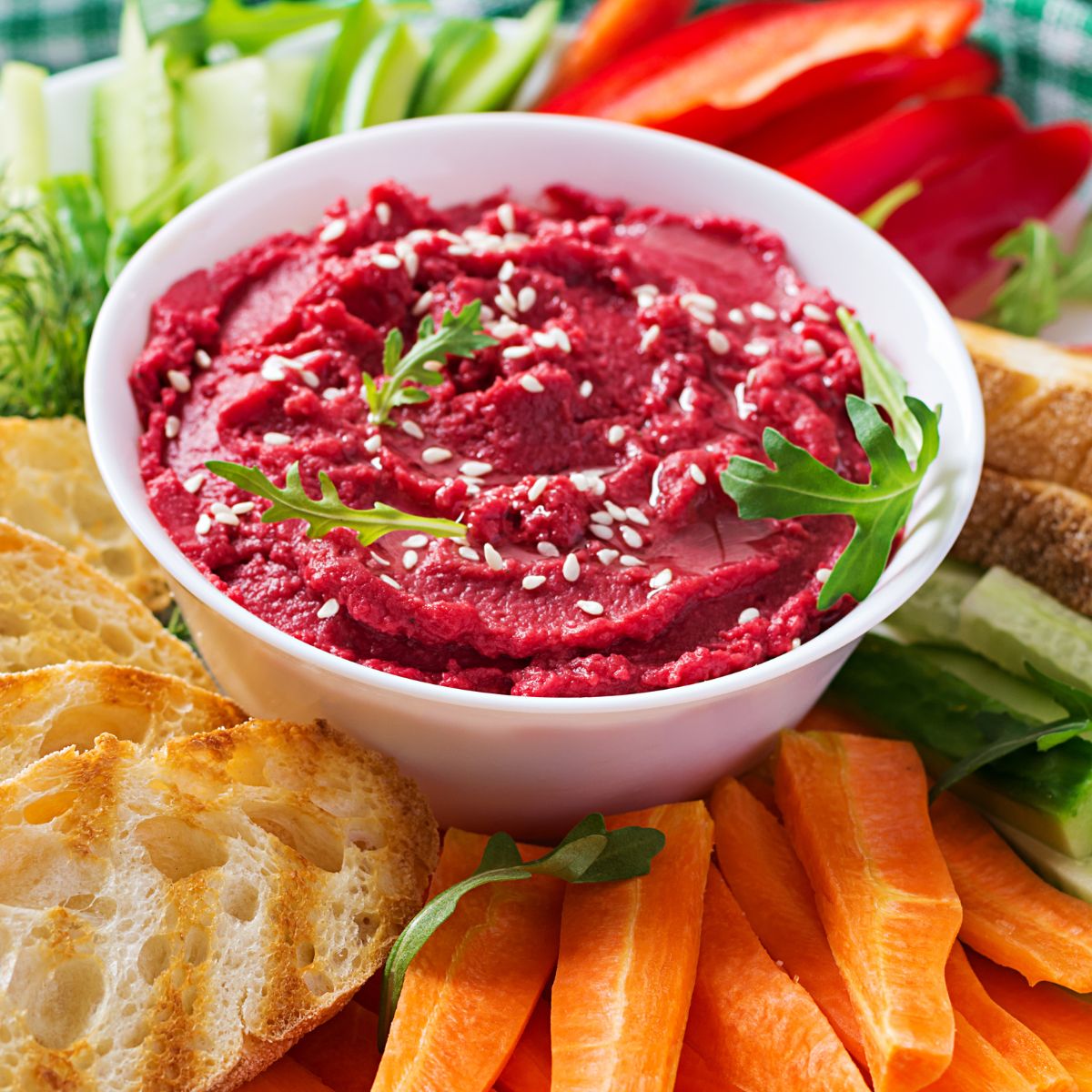 beet hummus in a white bowl surrounded by fresh veggies