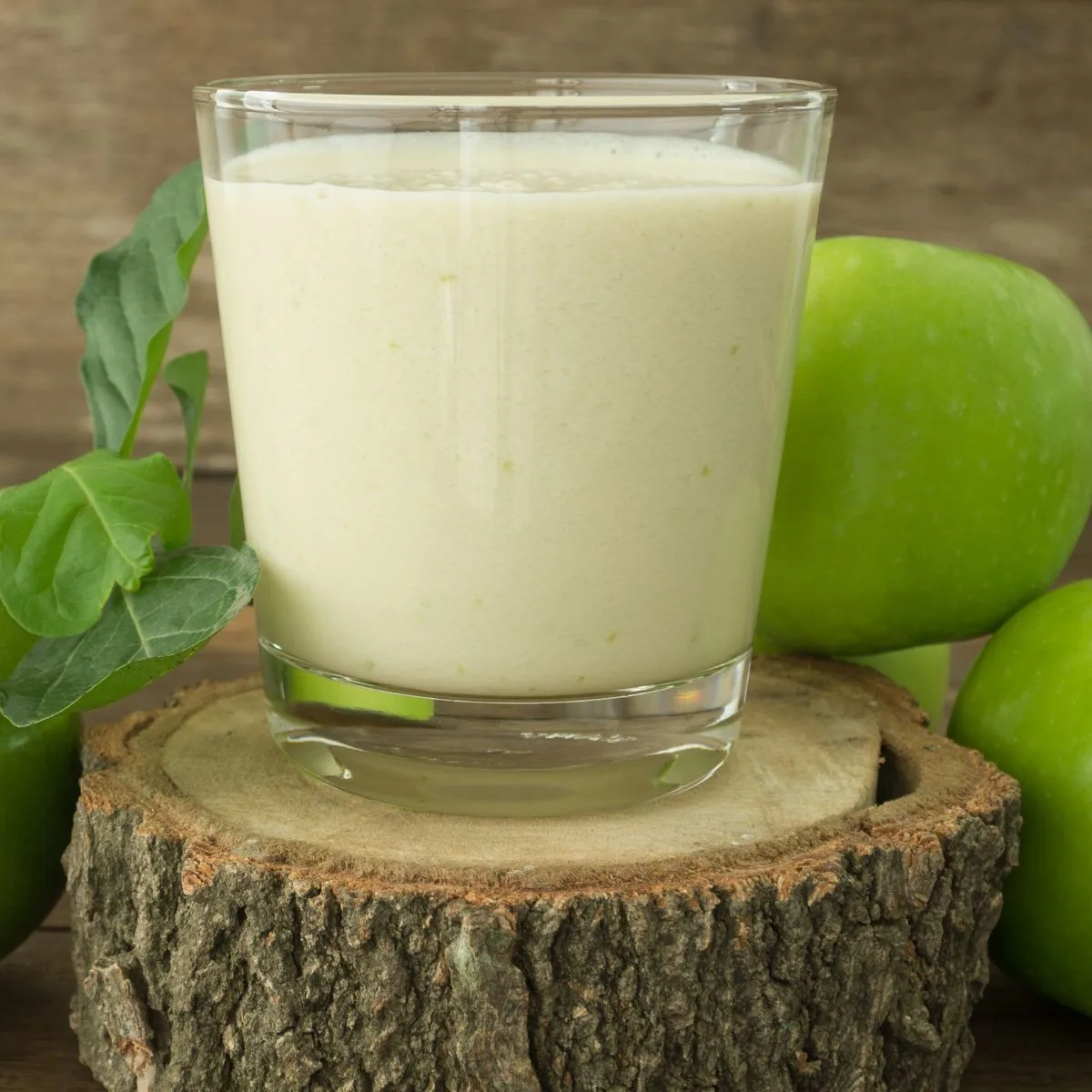 a glass of green apple smoothie on a wood slice