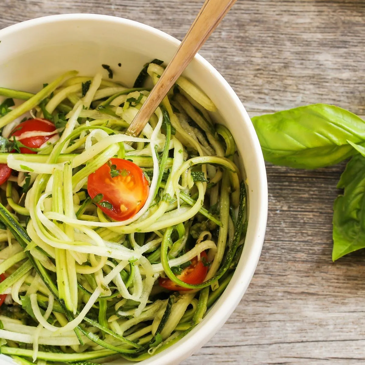 a bowl of zucchini noodle pasta with basil and cherry tomatoes
