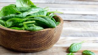 Fresh baby spinach in a wooden bowl on rustic wooden background, selective focus